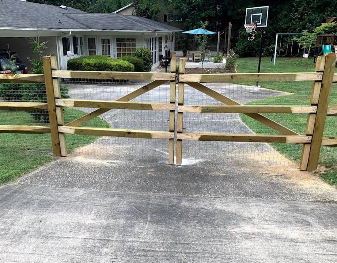 A wooden fence surrounds a driveway leading to a house.