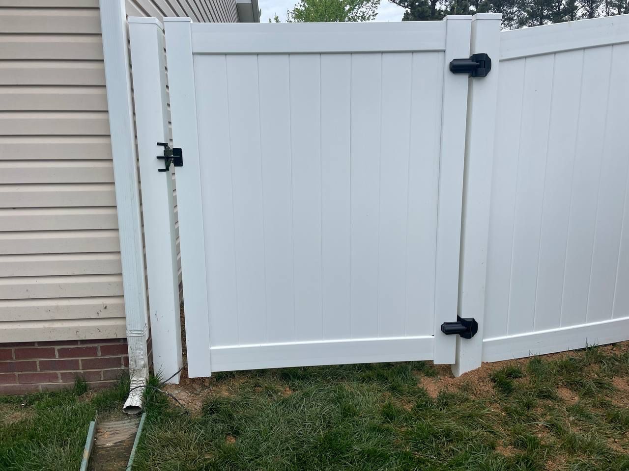 A white fence with a black gate is next to a house.