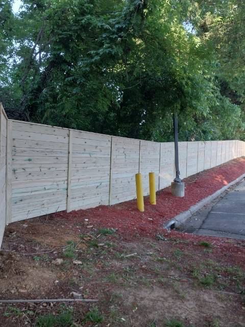 A wooden fence along a sidewalk next to a street.
