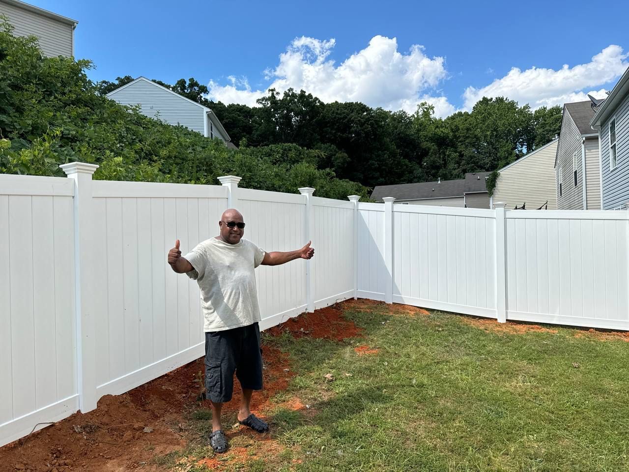 A man is standing in front of a white fence in a backyard.