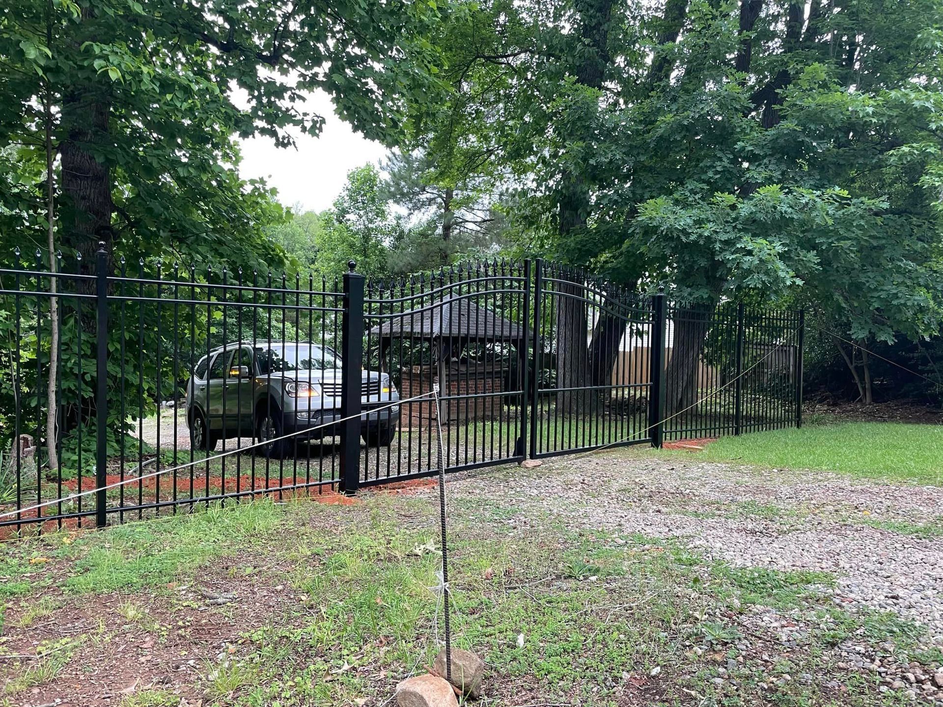 A car is parked in a driveway behind a wrought iron fence.