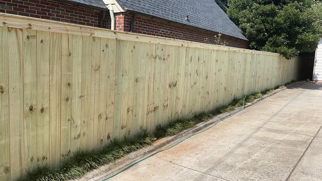 A wooden fence is along the side of a driveway next to a brick building.