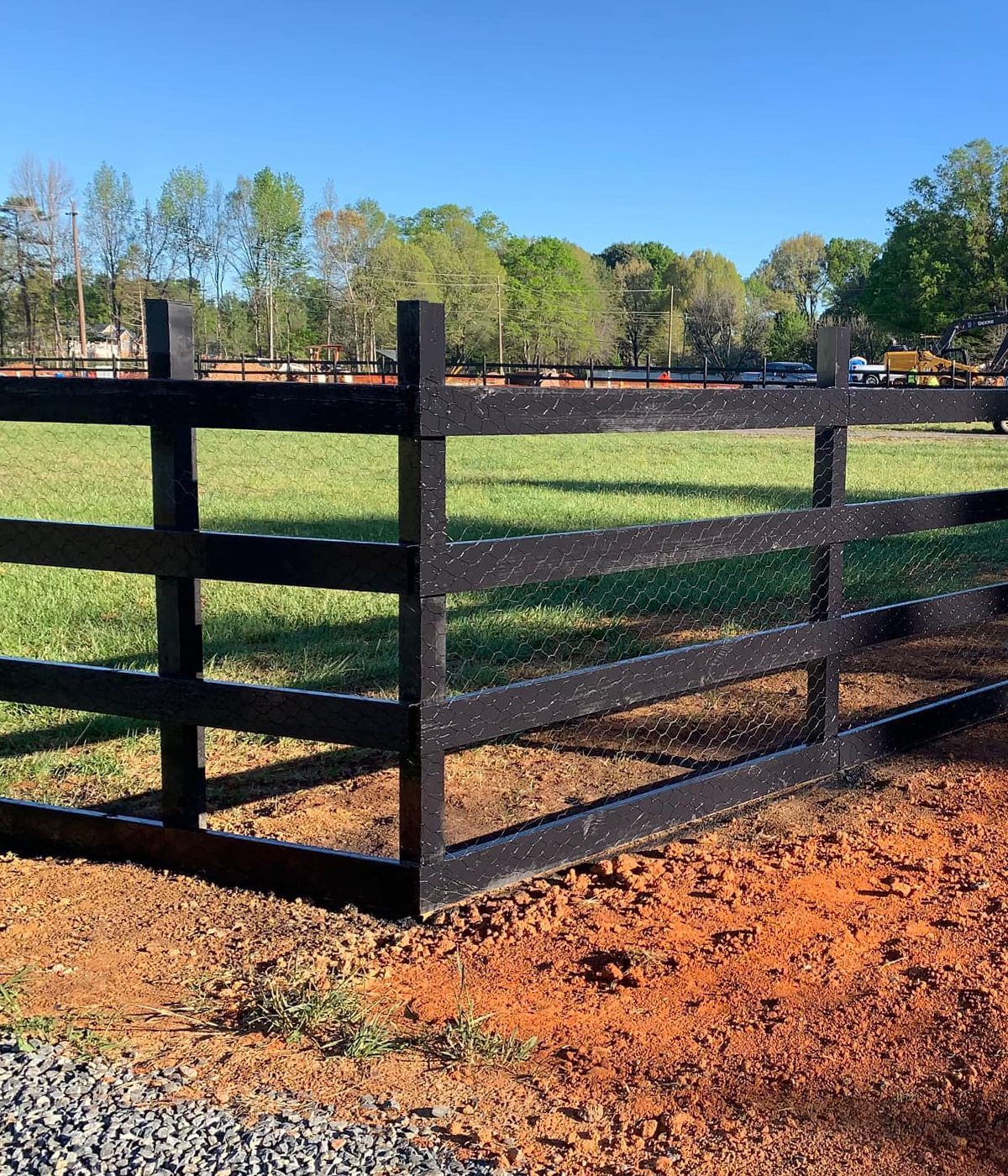 A black wooden fence surrounds a grassy field.