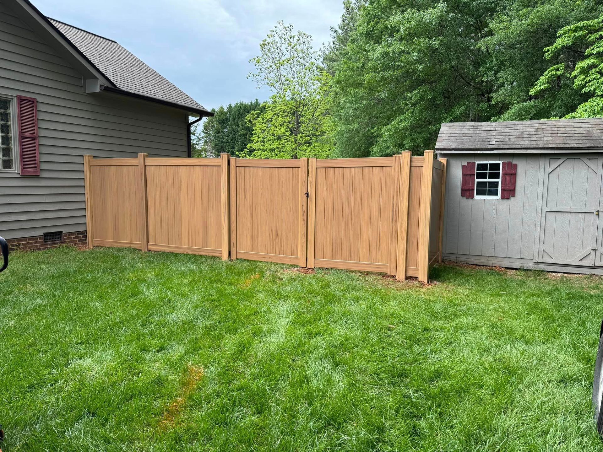 A wooden fence is in the backyard of a house next to a shed.