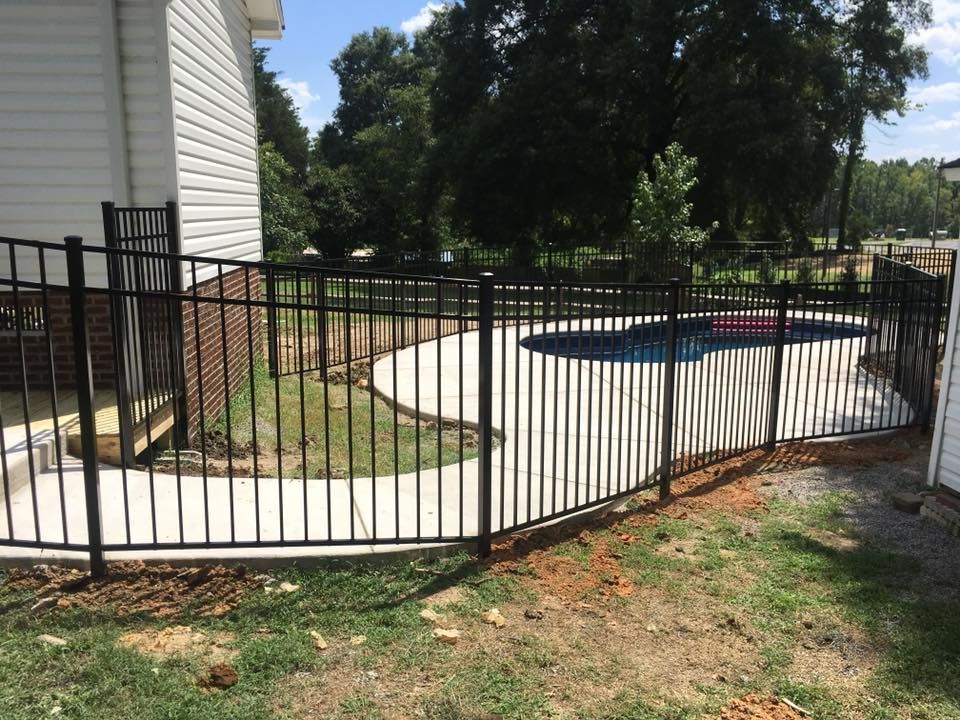 A black metal fence surrounds a swimming pool in a backyard.