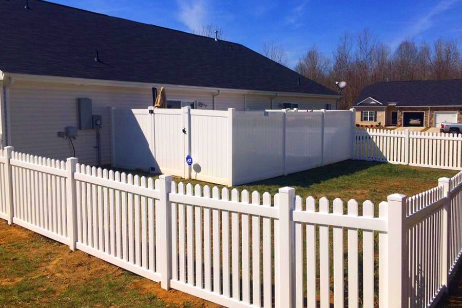 A white picket fence surrounds a yard in front of a house.