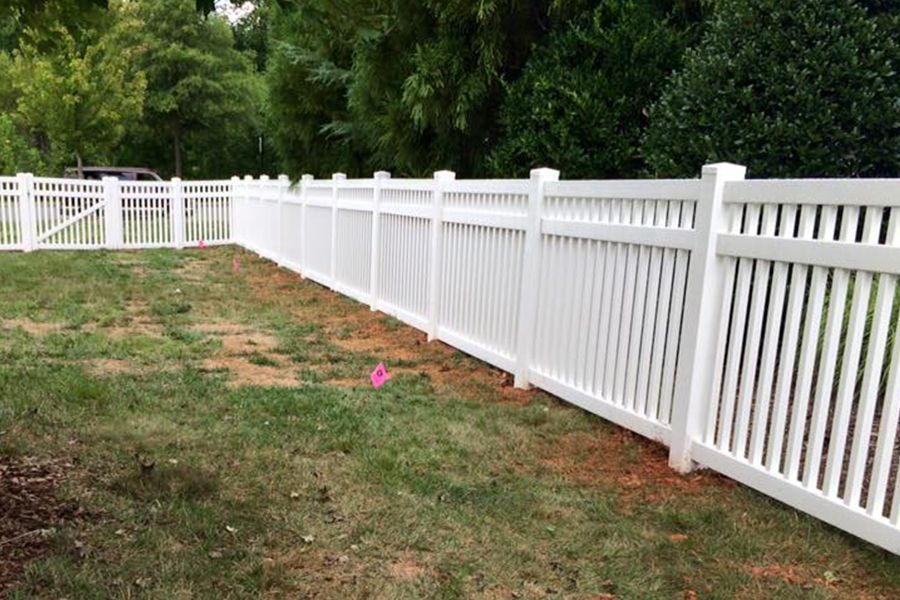 A white vinyl fence is sitting in the middle of a lush green yard.