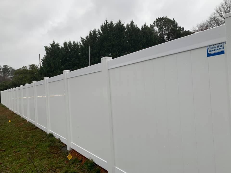 A white vinyl fence is sitting in the middle of a grassy field.