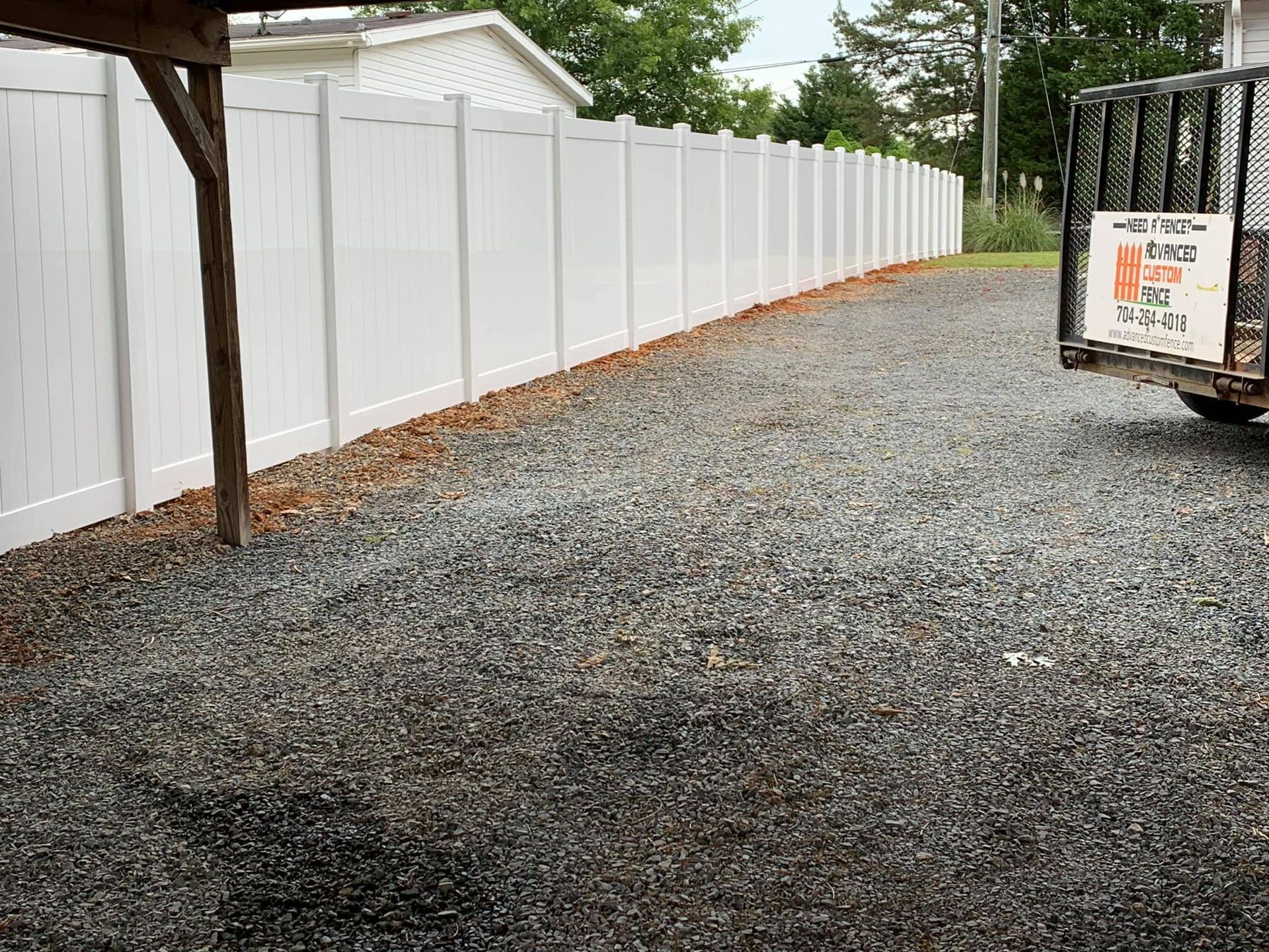 A white fence is surrounding a gravel driveway.