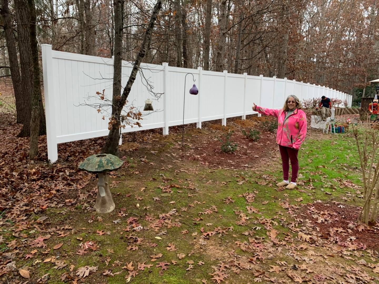 A woman in a pink jacket is standing in front of a white fence.