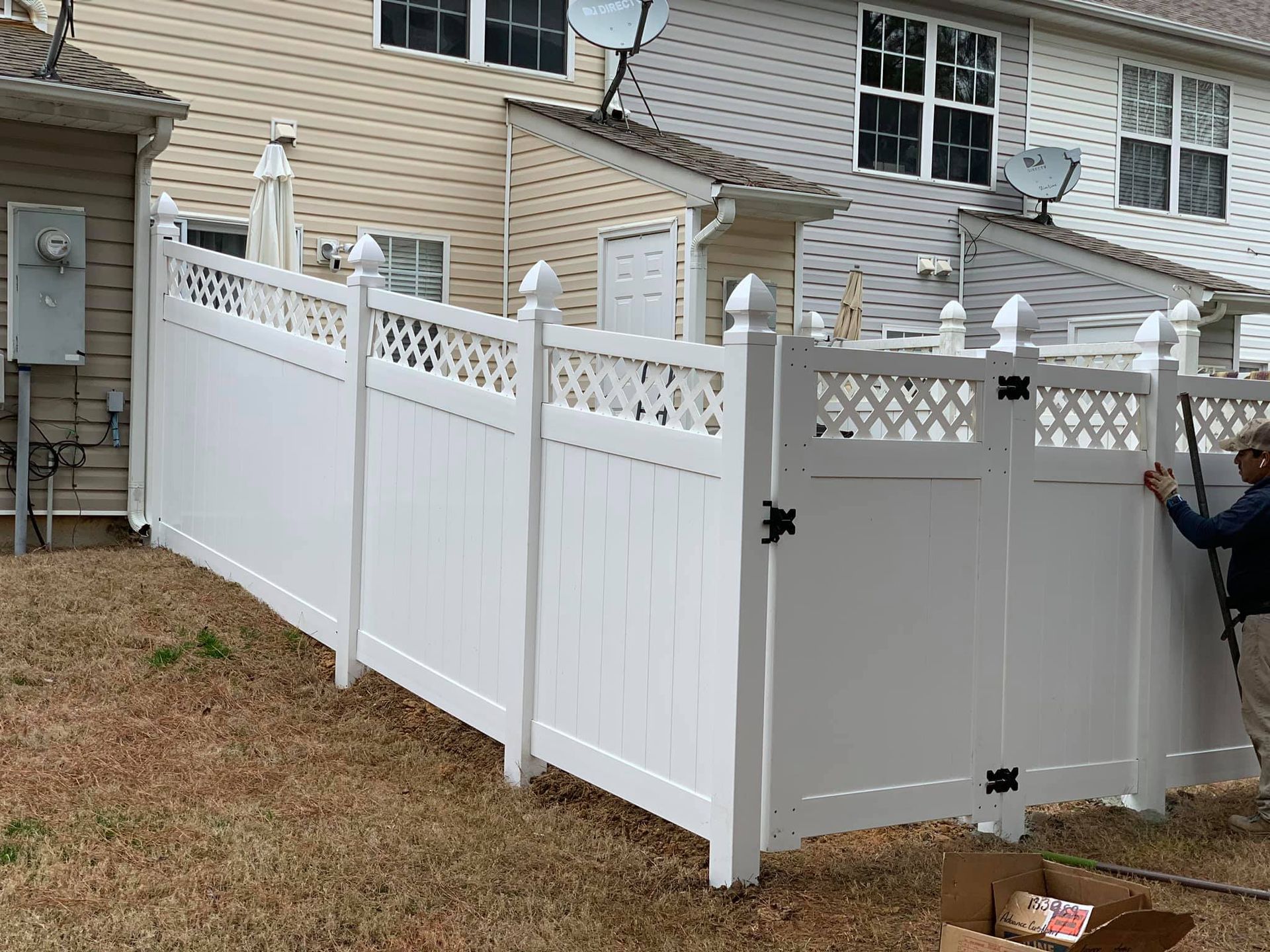 A man is standing next to a white fence in front of a house.