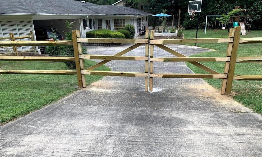 A wooden fence surrounds a driveway leading to a house.