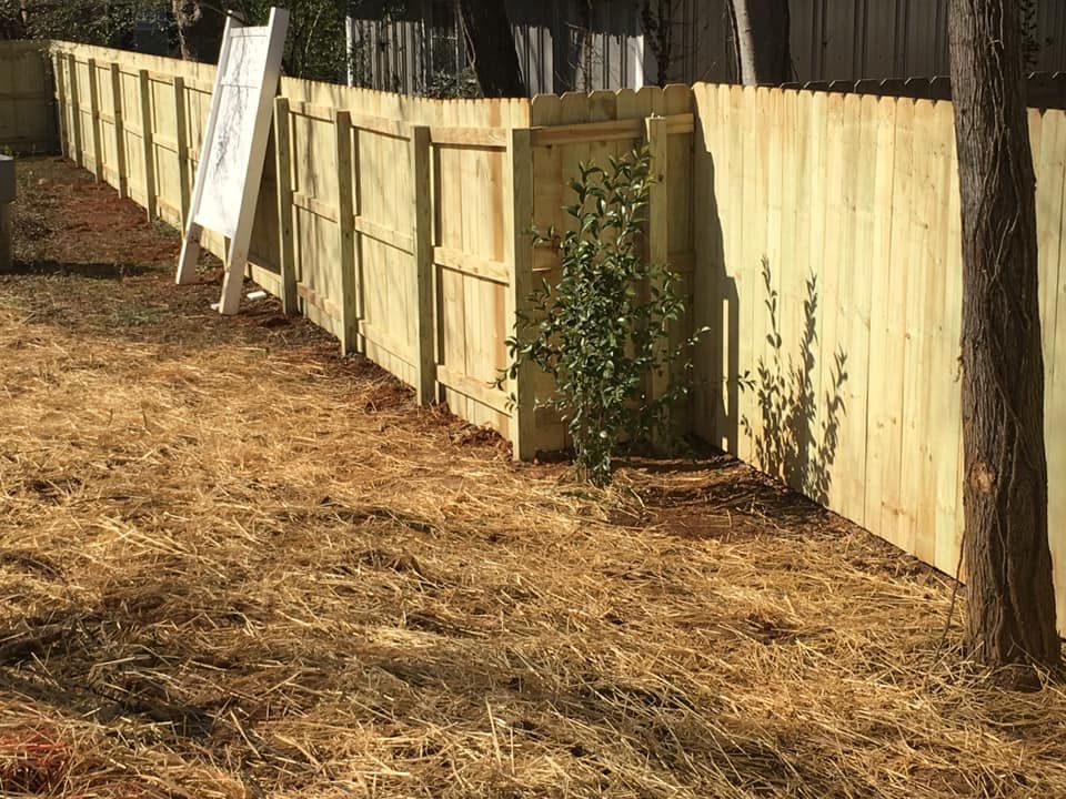 A wooden fence is surrounded by dry grass and trees in a yard.