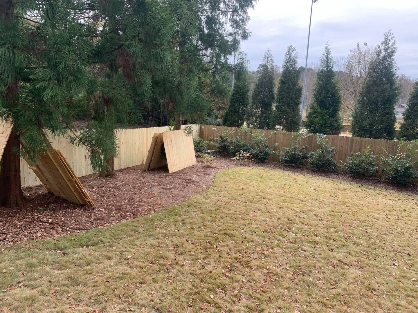 A large yard with a wooden fence and trees in the background.