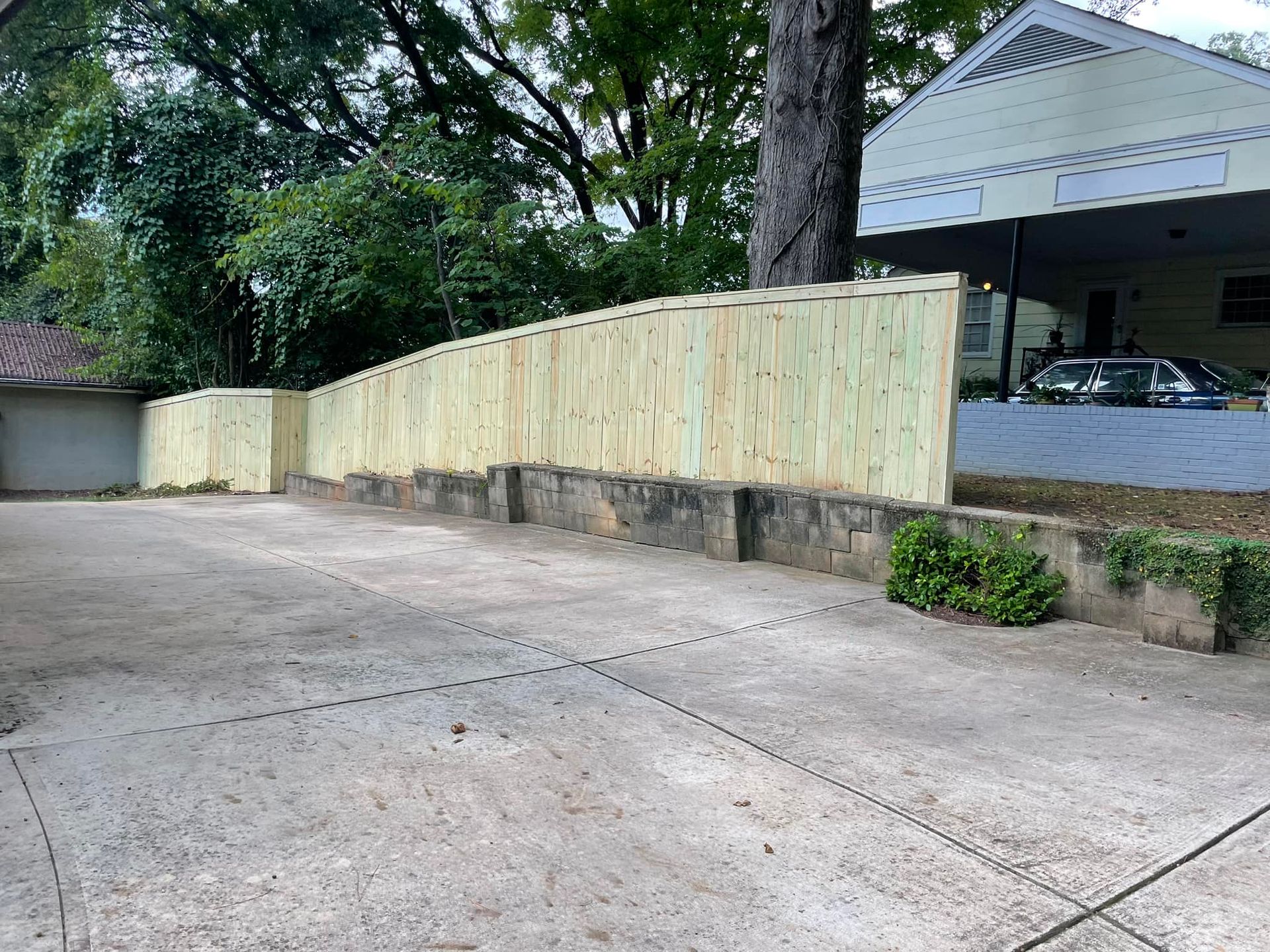 A wooden fence is surrounding a driveway in front of a house.