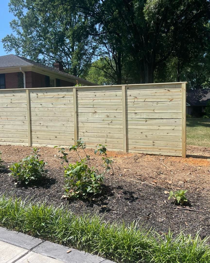 A wooden fence is sitting in the middle of a yard next to a house.