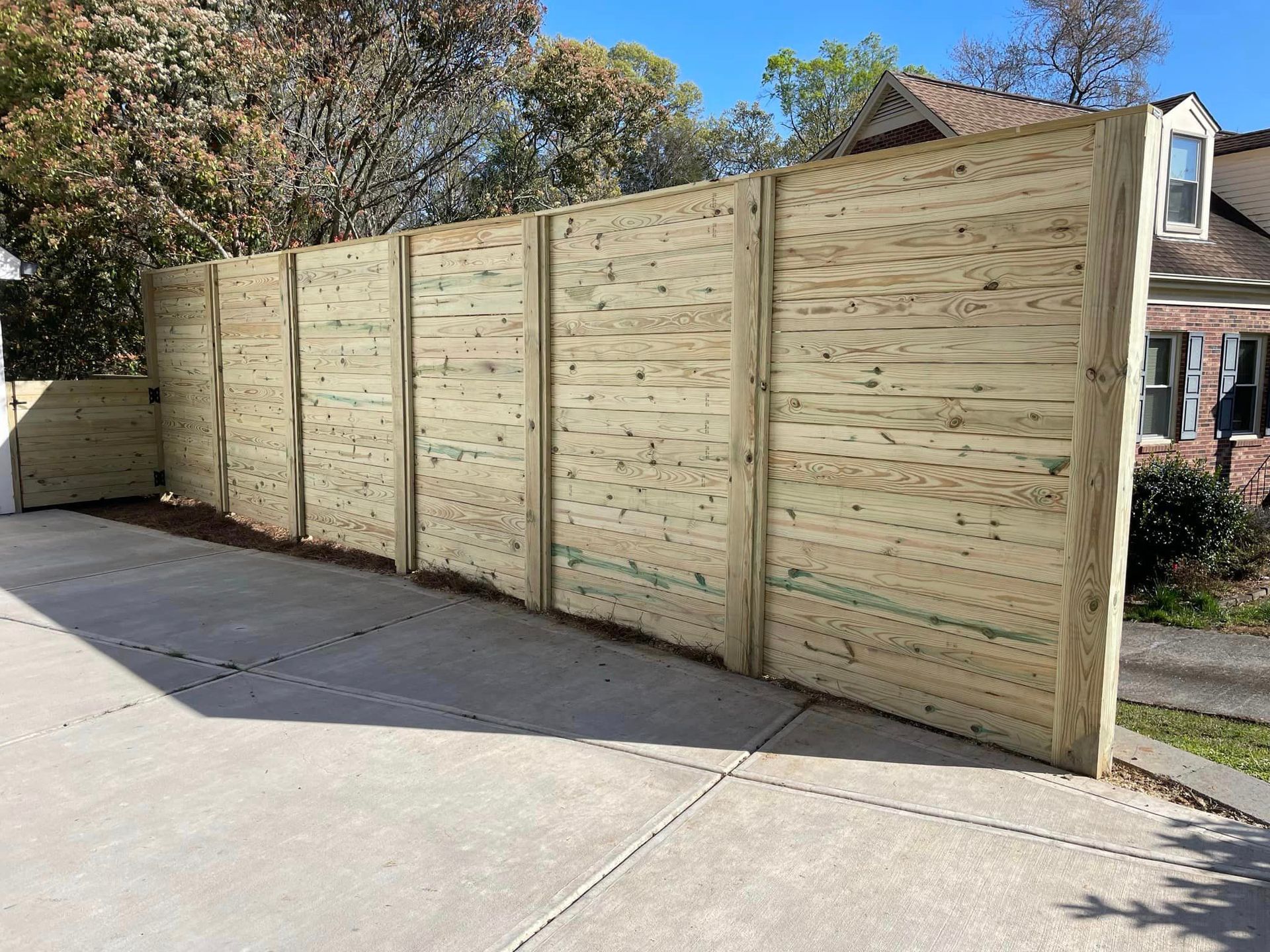 A wooden fence is sitting in the middle of a driveway next to a house.