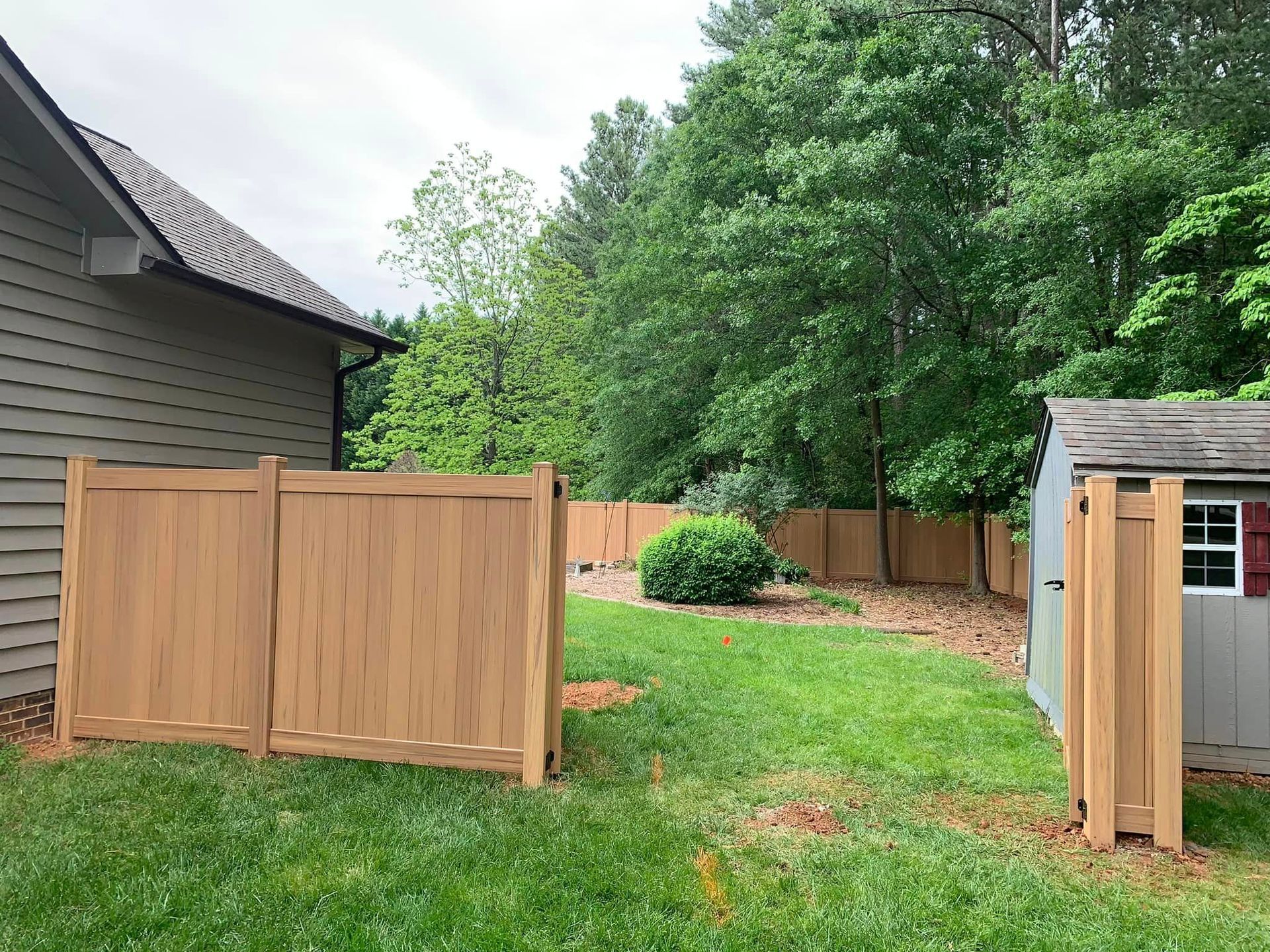 A wooden fence is in the backyard of a house next to a shed.