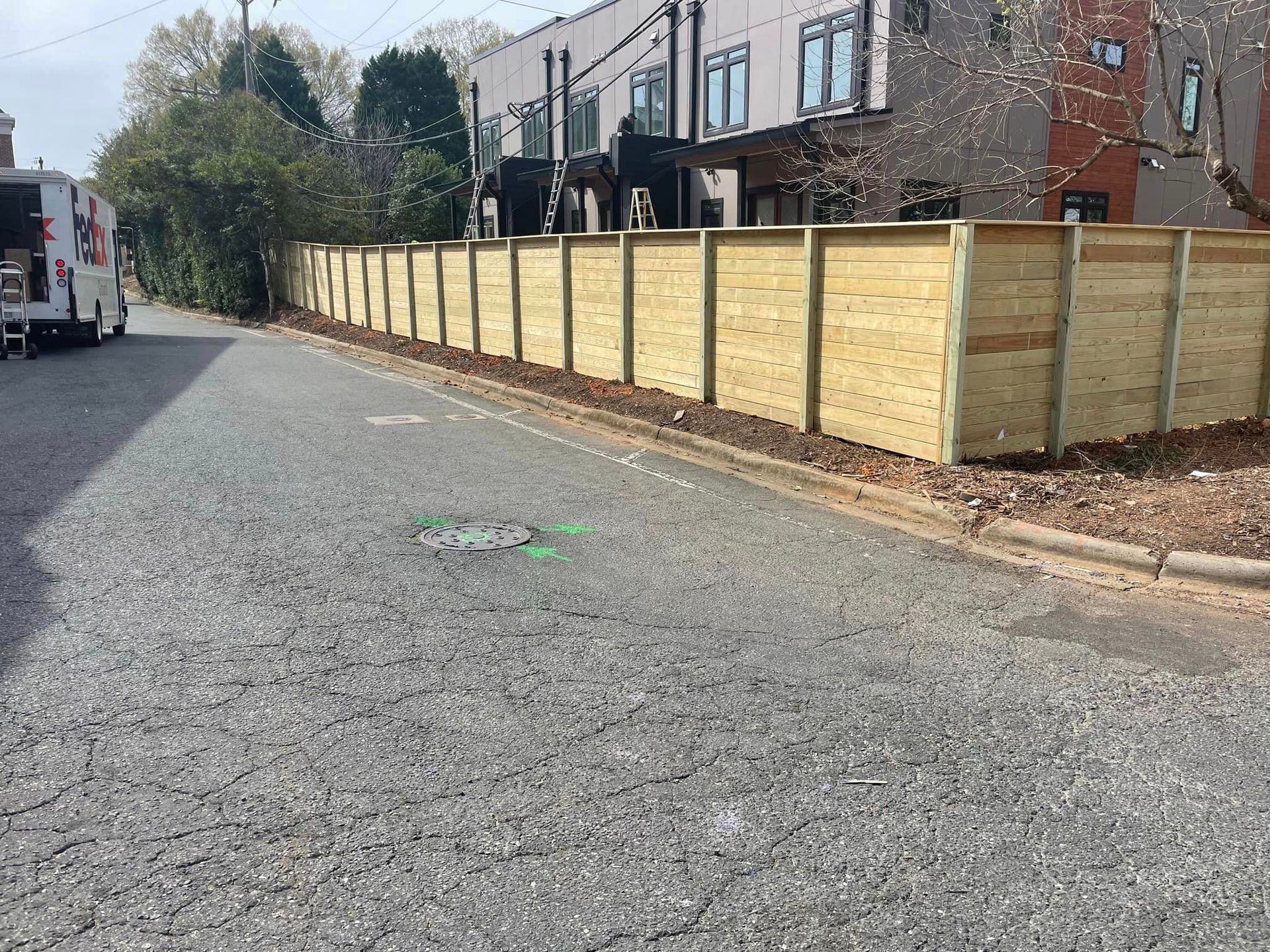 A wooden fence is along the side of a road.