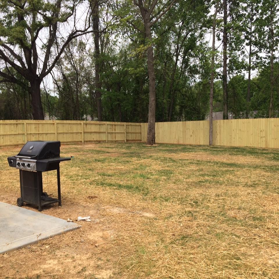A grill is sitting in the middle of a yard next to a wooden fence.