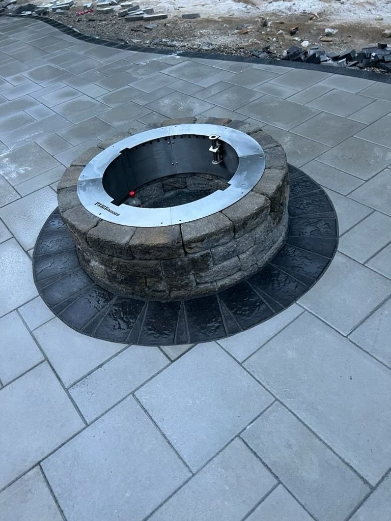 A circular stone fire pit with a steel rim set in the center of a gray stone patio.