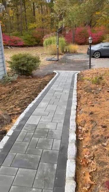A new stone walkway with a gray patterned center and dark border, edged with light gray rocks in an autumn yard.