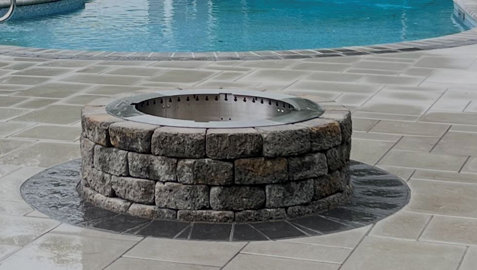 A fire pit is sitting on a patio next to a pool.
