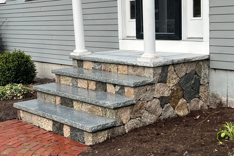 A stone porch with steps leading to the front door of a house.