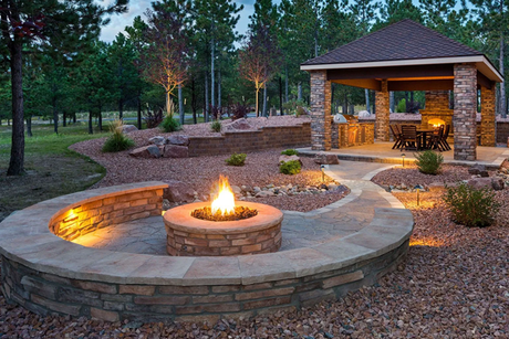A fire pit in a backyard with a gazebo in the background.
