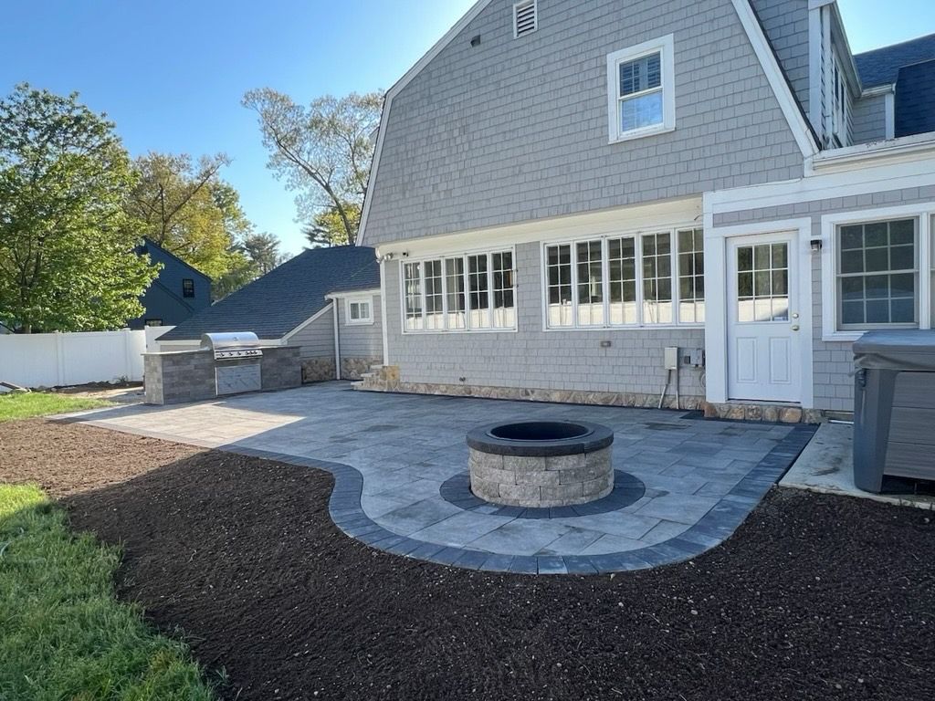 Backyard patio with fire pit, gray pavers, and house with shingled exterior.