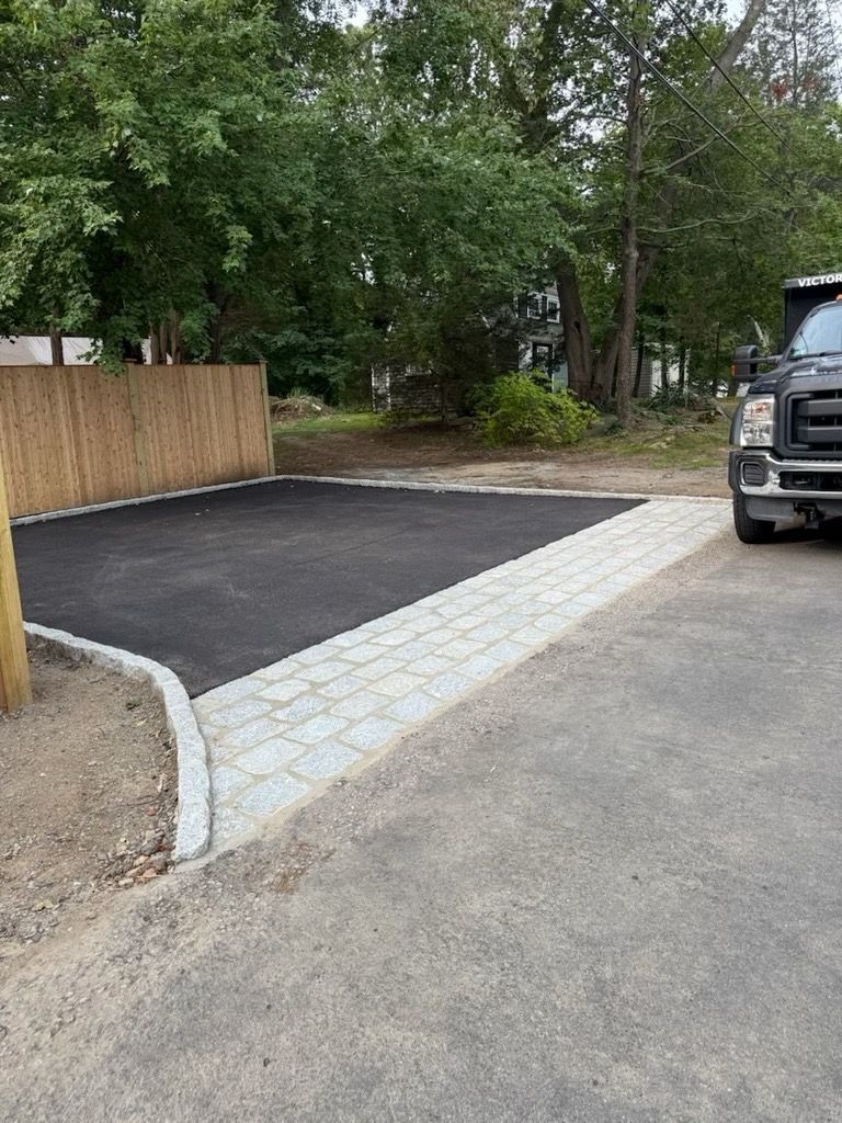 Newly paved driveway with gray pavers and black asphalt. A truck is parked to the right.