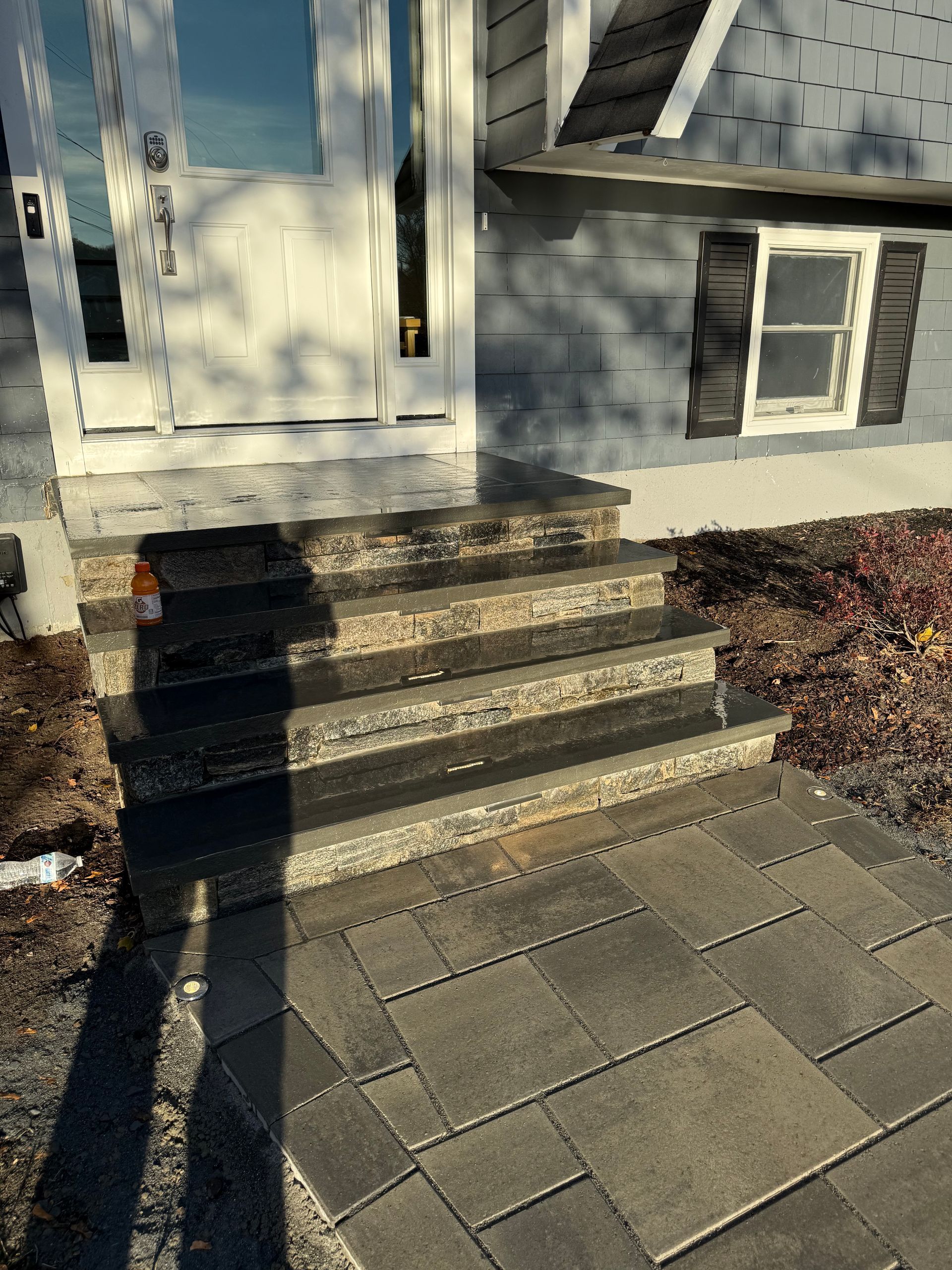 Gray stone steps leading up to a white door, with a patterned stone patio below.