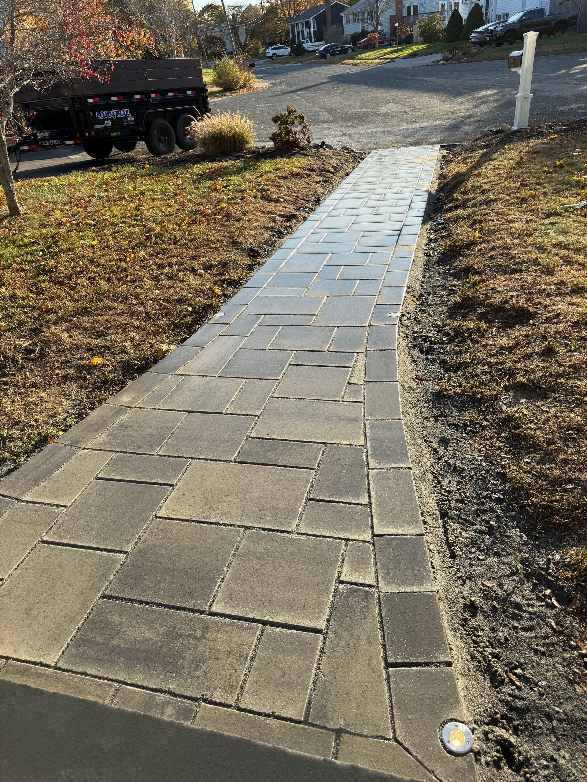 Brick paver walkway leading uphill, surrounded by grass and gravel.
