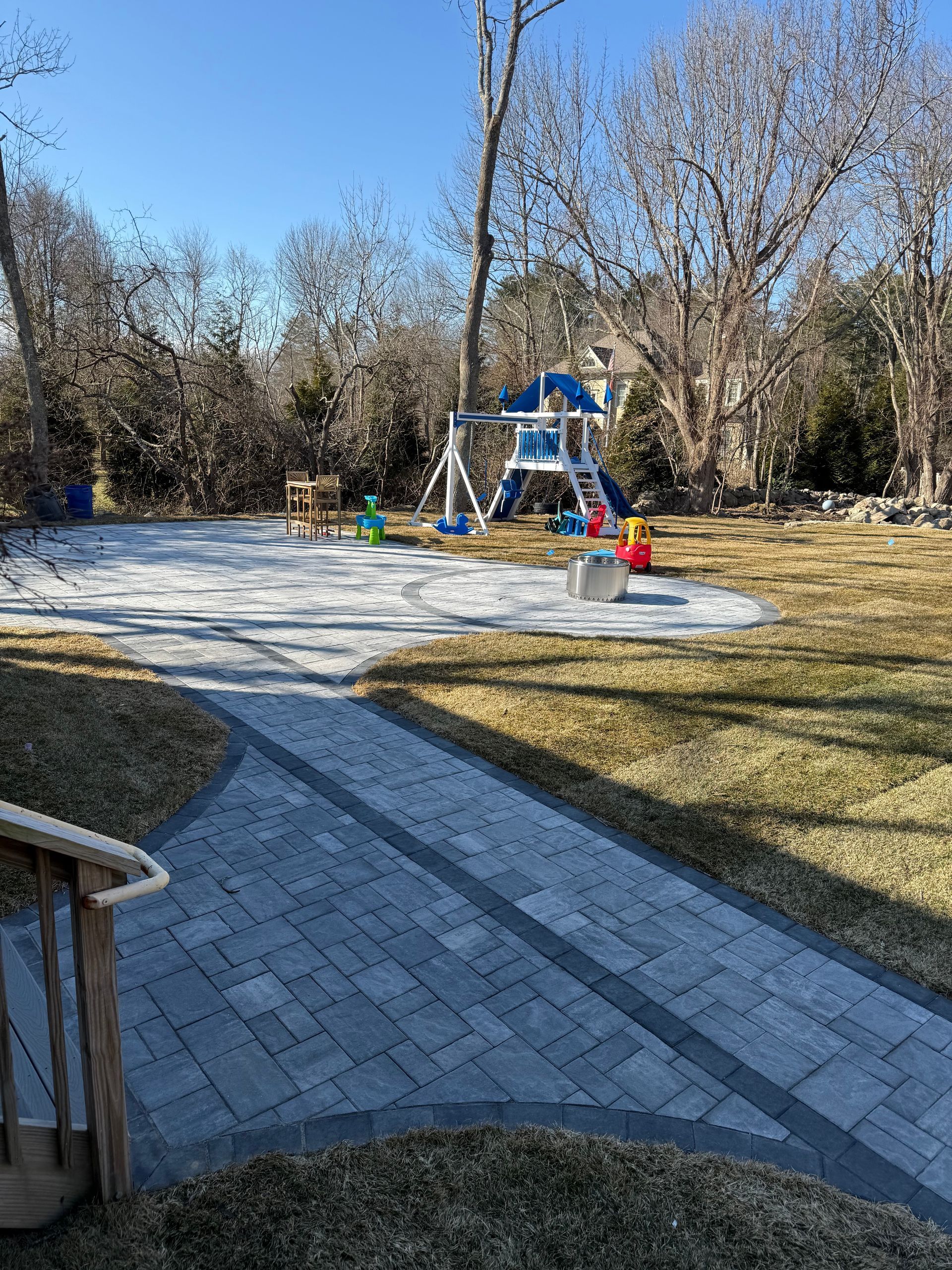 Backyard with brick path leading to playground, swingset, on gravel, sunny day.