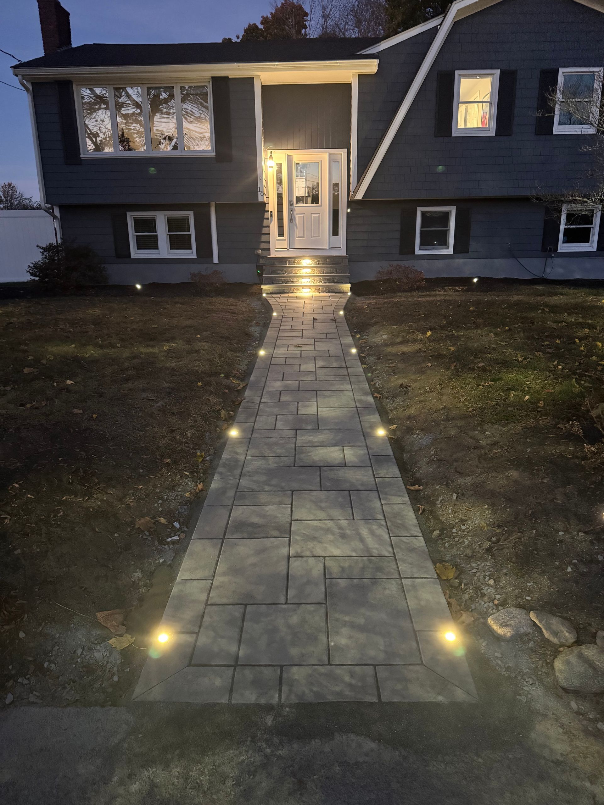 Night view of a gray house with a lighted walkway leading to the front door.