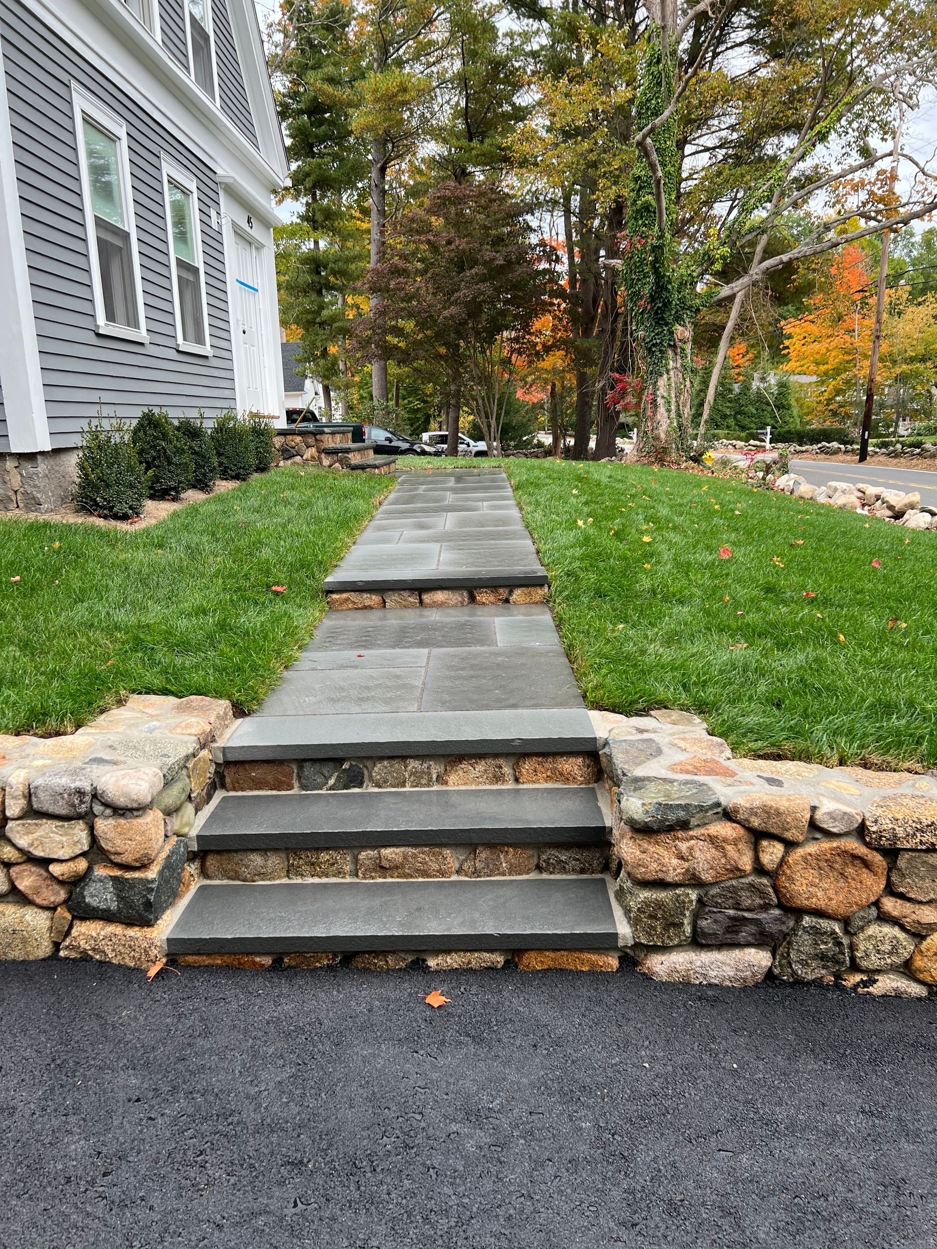 Stone steps with stone retaining walls, leading up to a house with fresh green grass.