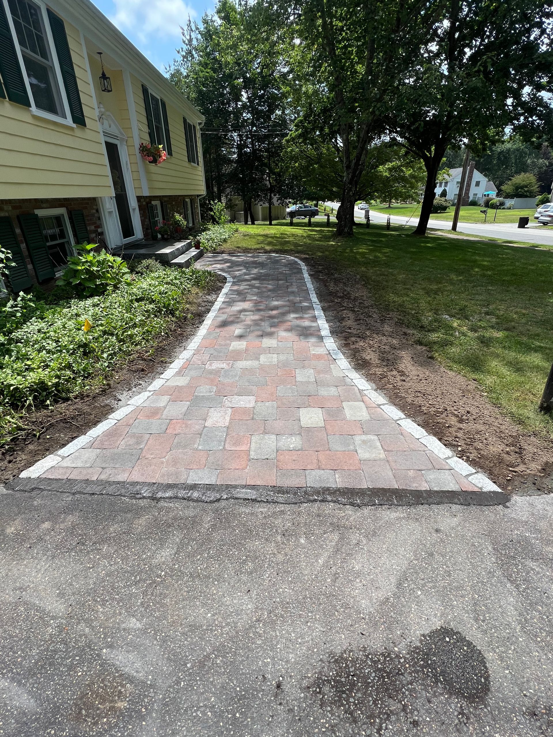 Brick walkway leading from driveway to a yellow house with a landscaped front yard.
