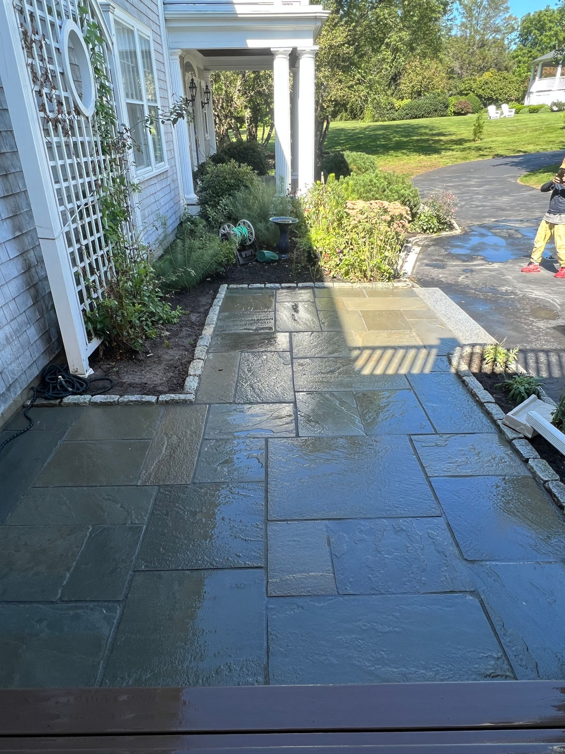 Wet stone patio outside a house with a person on the right and landscaping.