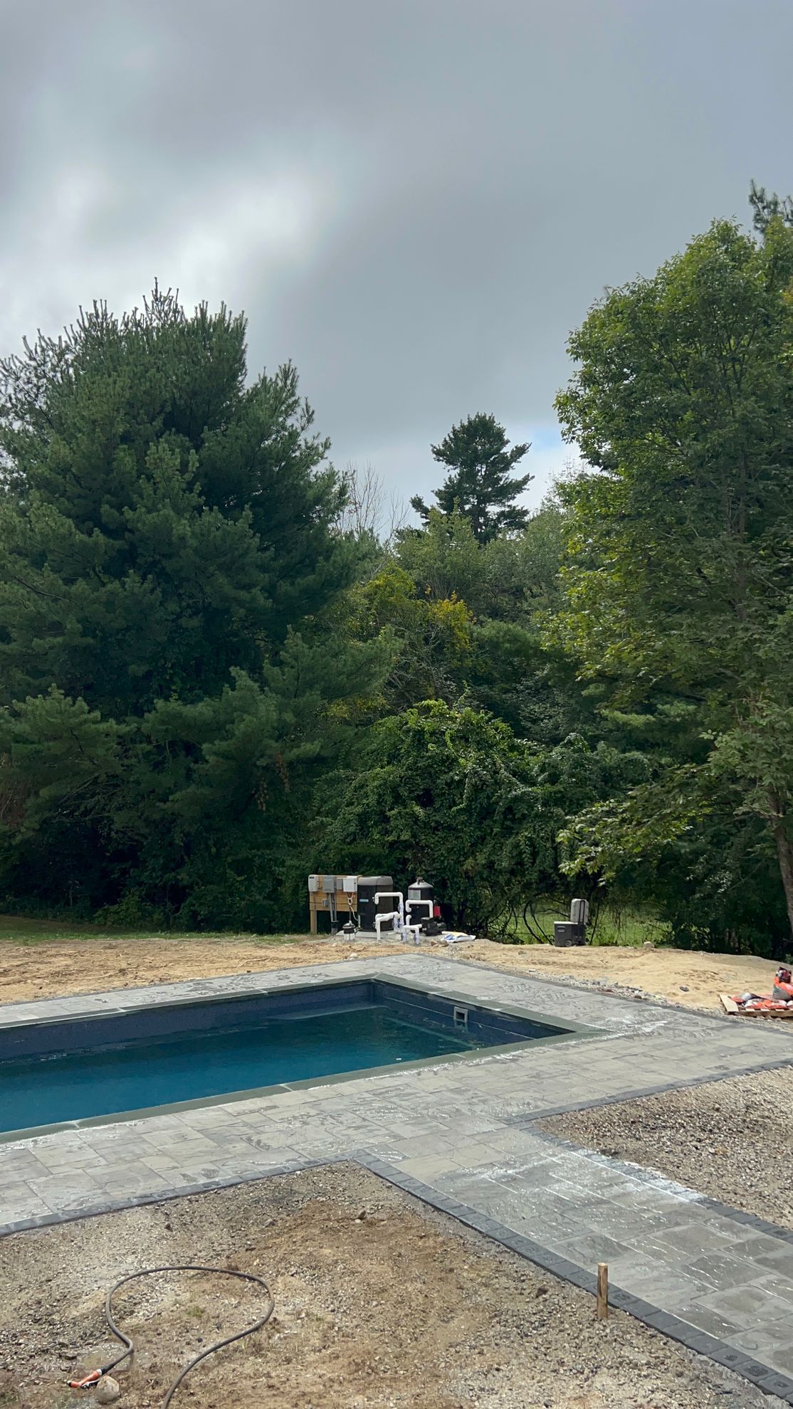 Pool construction in a backyard with trees and an overcast sky.