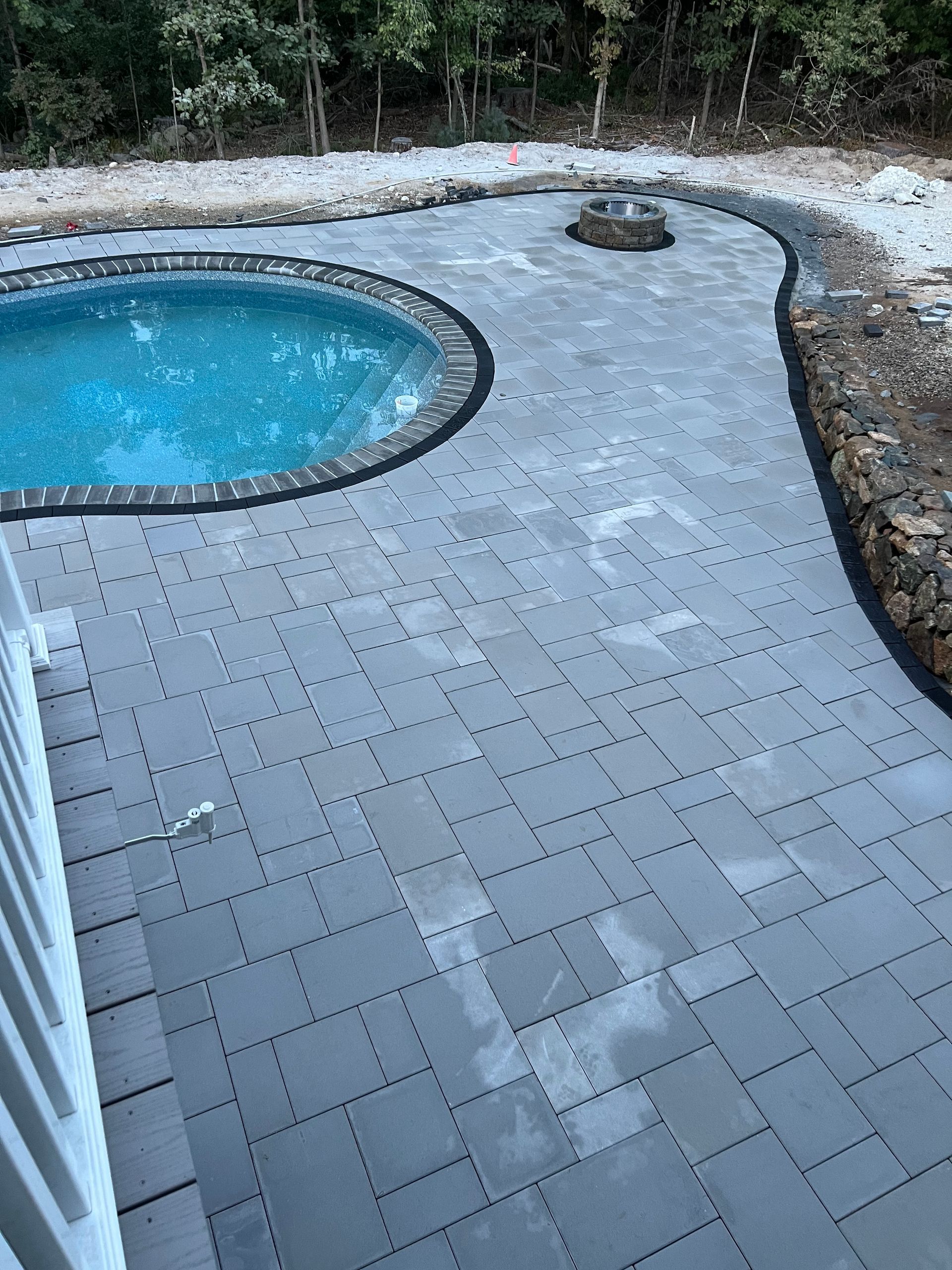 A pool with gray pavers, a fire pit, and a stone border.