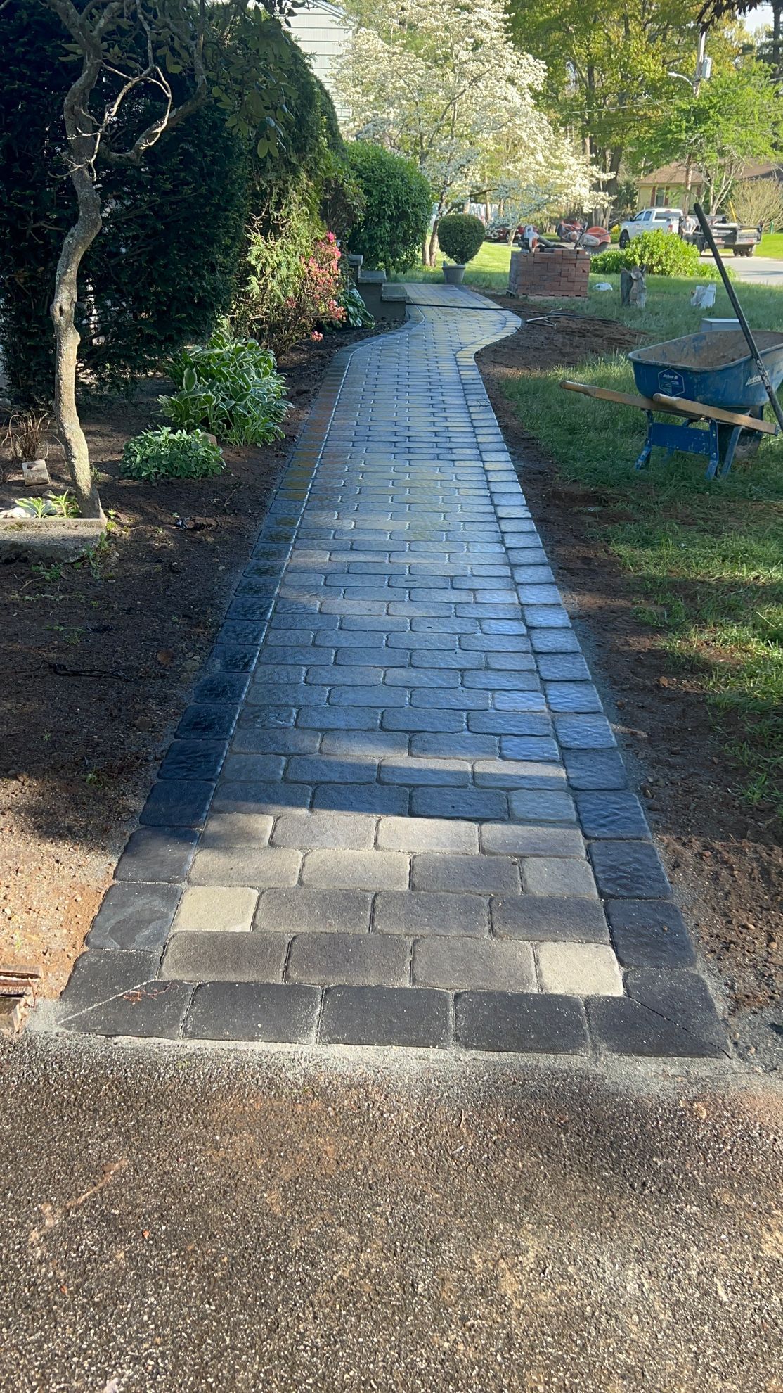 Brick pathway leading through a yard, bordered by dark bricks, garden, and grass.