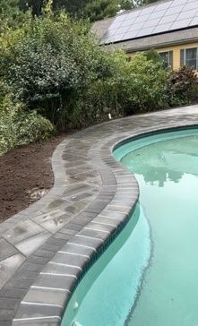 Curved pool edge with dark pavers, turquoise water, and greenery in the background.