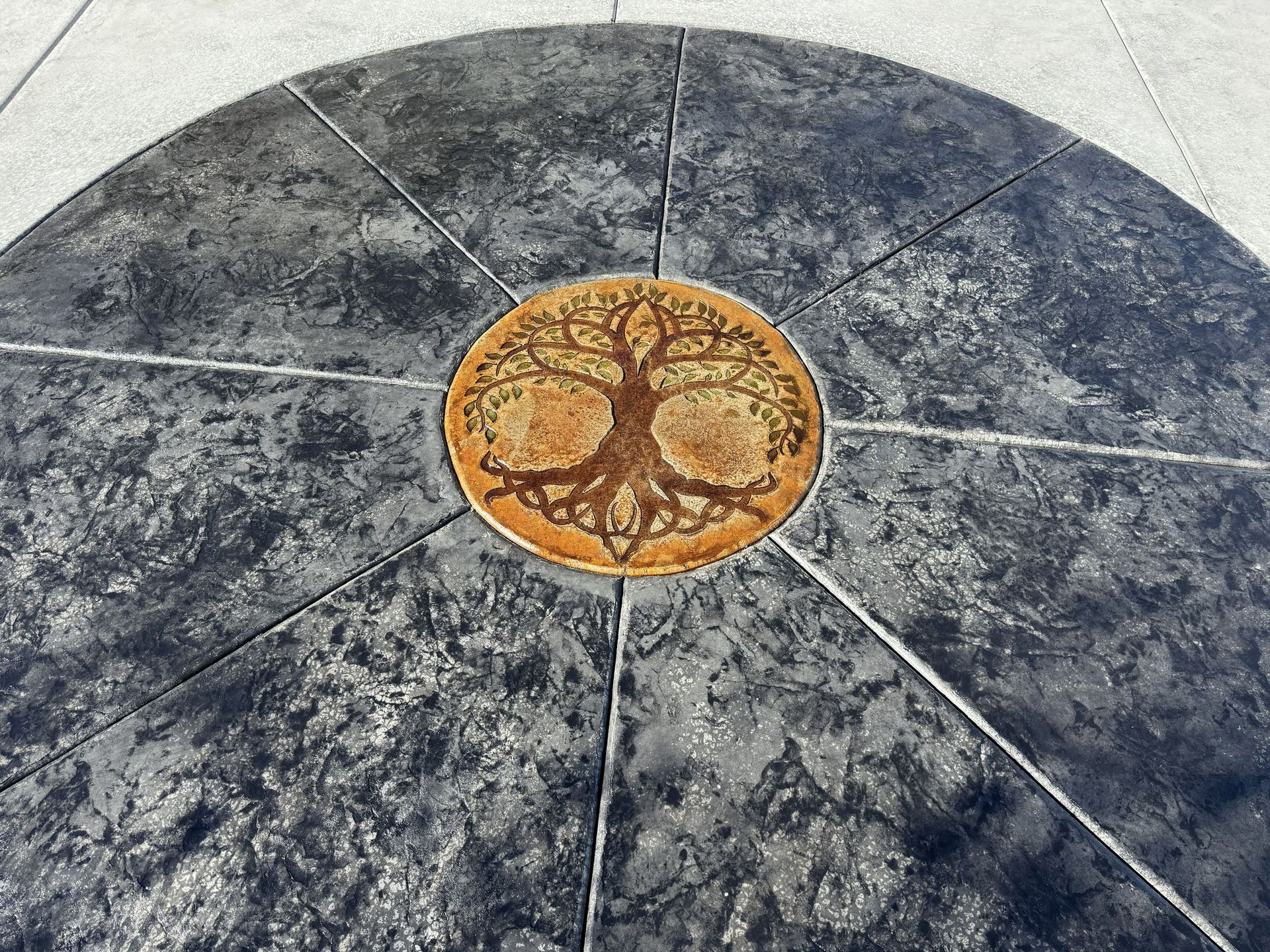 Circular concrete patio with tree of life design in the center, surrounded by lines.