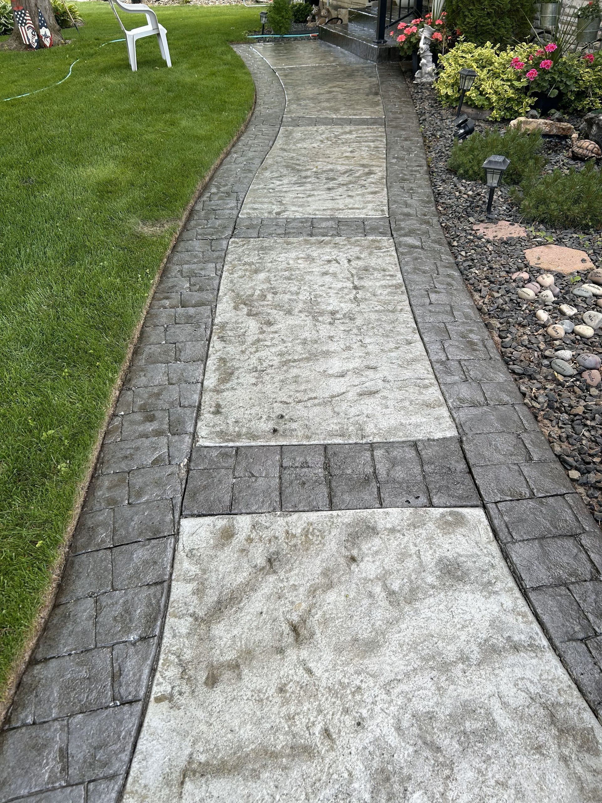 A brick walkway leads to a lawn with a white chair in the background.