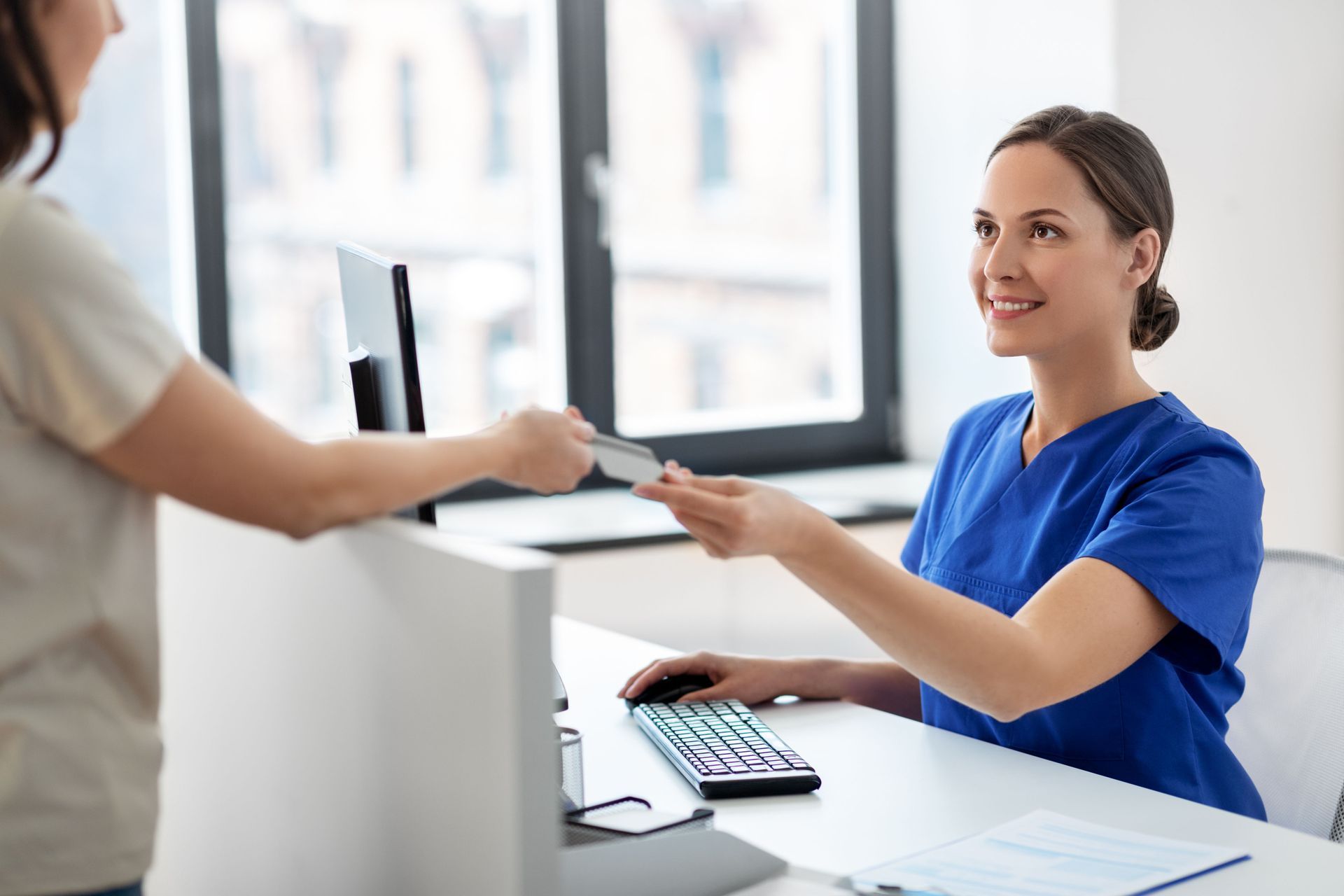 A nurse is giving a patient a card at a reception desk.