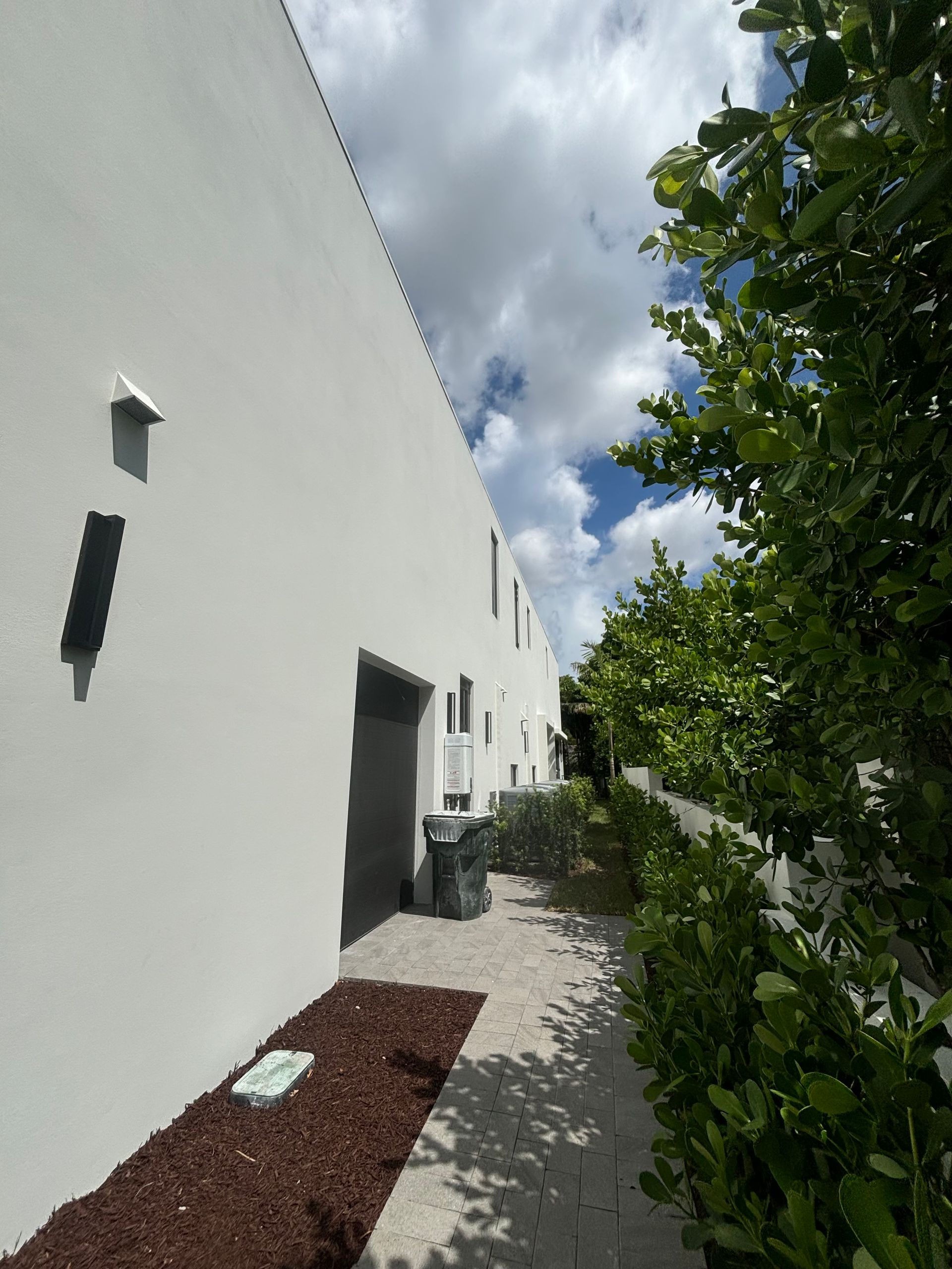 A white building with a walkway leading to it surrounded by trees and bushes.