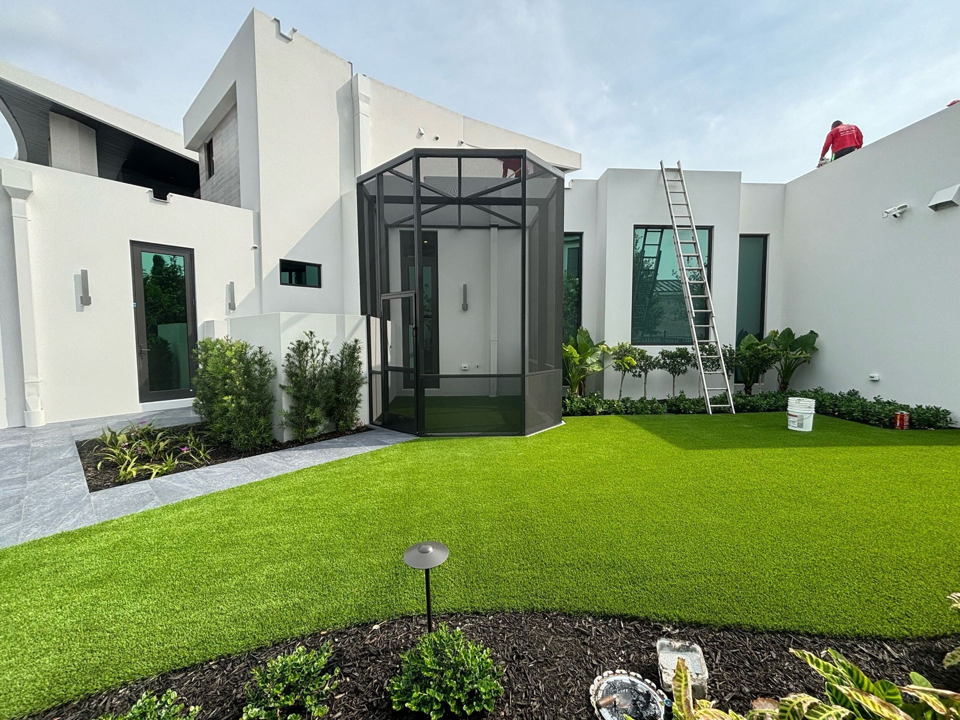 A man is painting the roof of a house with a ladder.