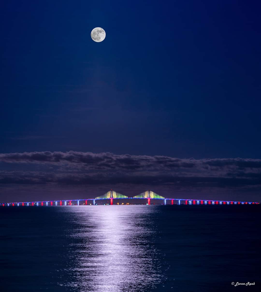 A full moon rises over a bridge over a body of water
