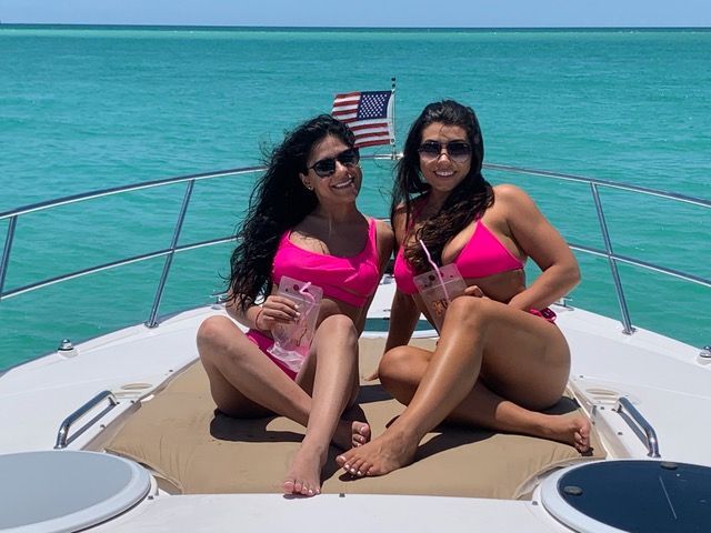 Two women in pink bikinis are sitting on a boat in the ocean.