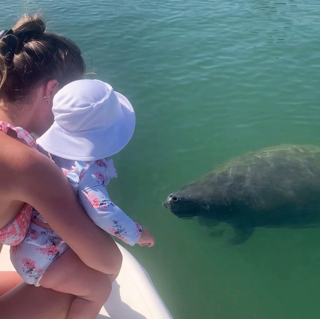 A woman and child are looking at a manatee in the water